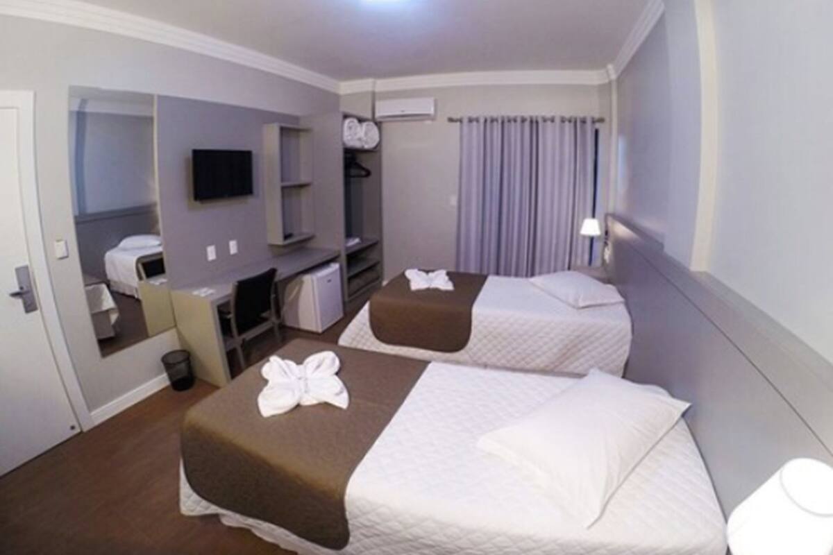 Habitación de hotel con dos camas, un escritorio, una silla, un televisor, un armario y una ventana con cortinas.