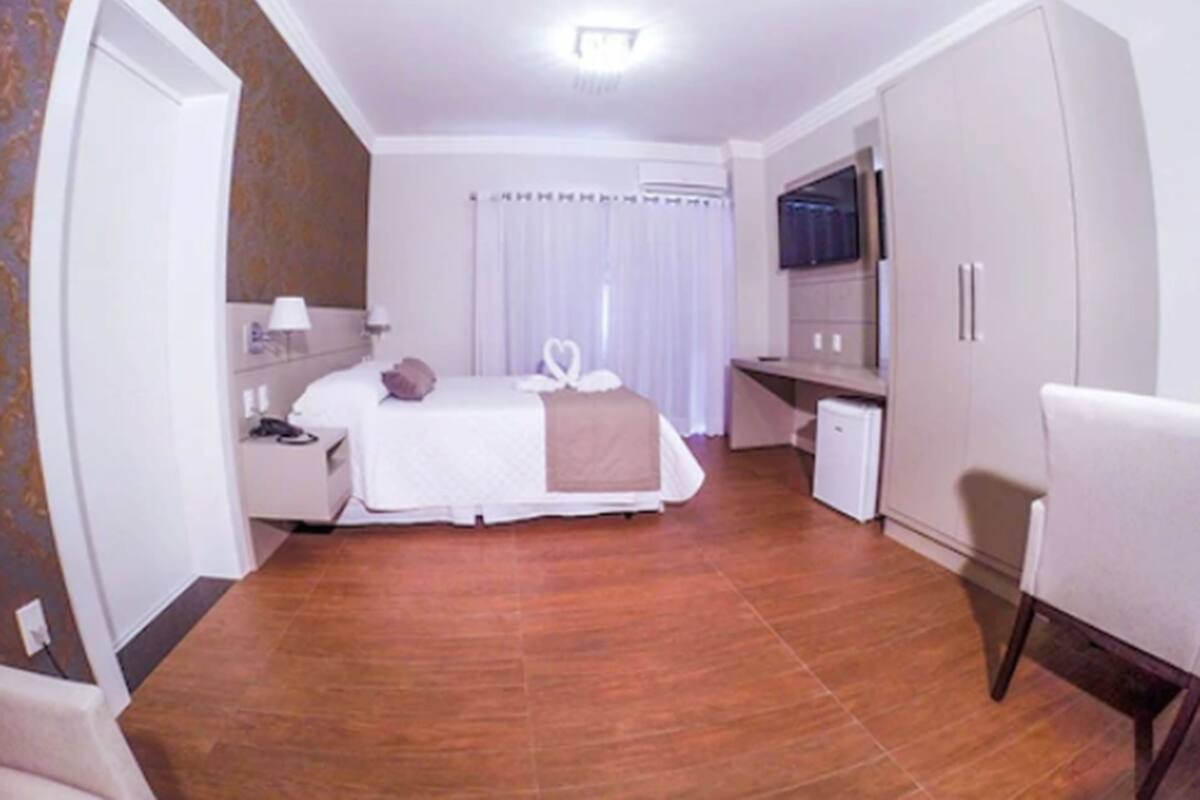 Habitación de hotel con cama, mesita de noche, lámpara y escritorio con silla.
