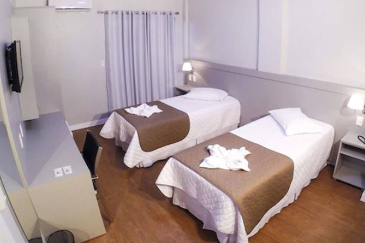 Una habitación de hotel con dos camas, un escritorio, una silla, una lámpara y un televisor.