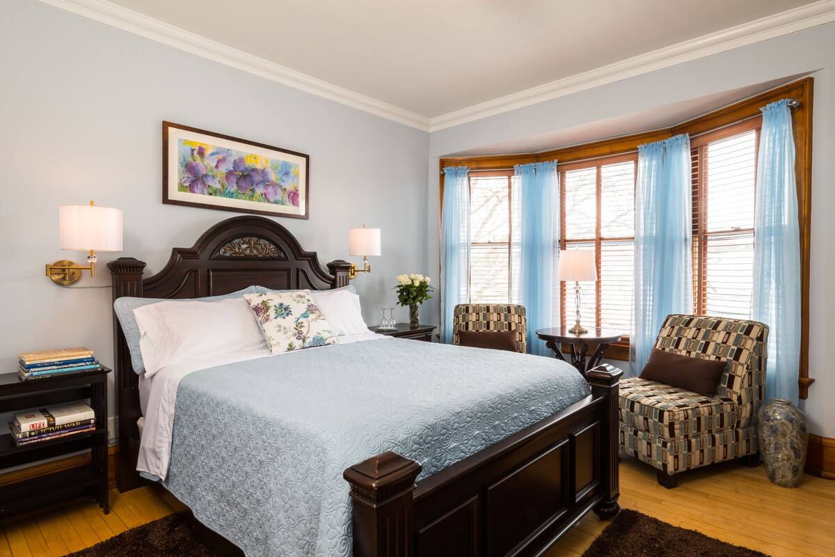 A bedroom with a large bed, a chair, a small table, and a vase.