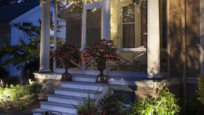 A two-story house with a covered porch, columns, and a garden with potted plants and a bench. - Honeybee Inn Bed & Breakfast (Horicon)