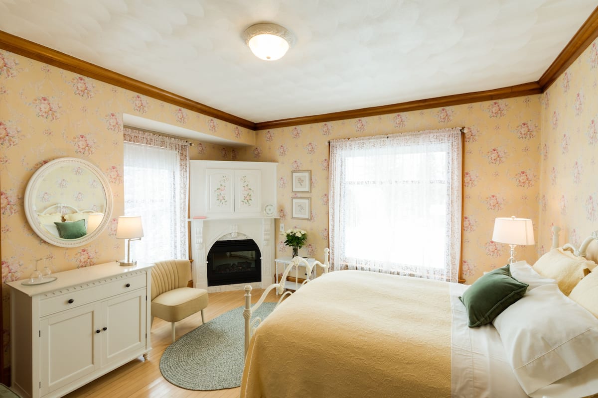 A bedroom with a bed, dresser, chair, and fireplace.
