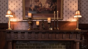 A fireplace with a fire, a framed painting above it, and two lamps on either side. - Honeybee Inn Bed & Breakfast (Horicon)