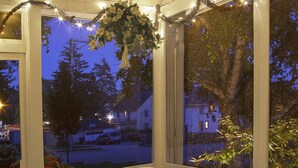 A covered patio with a table and chairs, a hanging floral arrangement, and a view of the neighborhood at dusk. - Honeybee Inn Bed & Breakfast (Horicon)