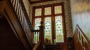 A wooden staircase with a balustrade, a floral wallpapered wall, and a stained glass window with floral patterns. - Honeybee Inn Bed & Breakfast (Horicon)