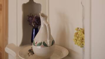 A white ceramic pitcher on a plate, a candle in a wall-mounted holder, and a shadow of a person on the wall.