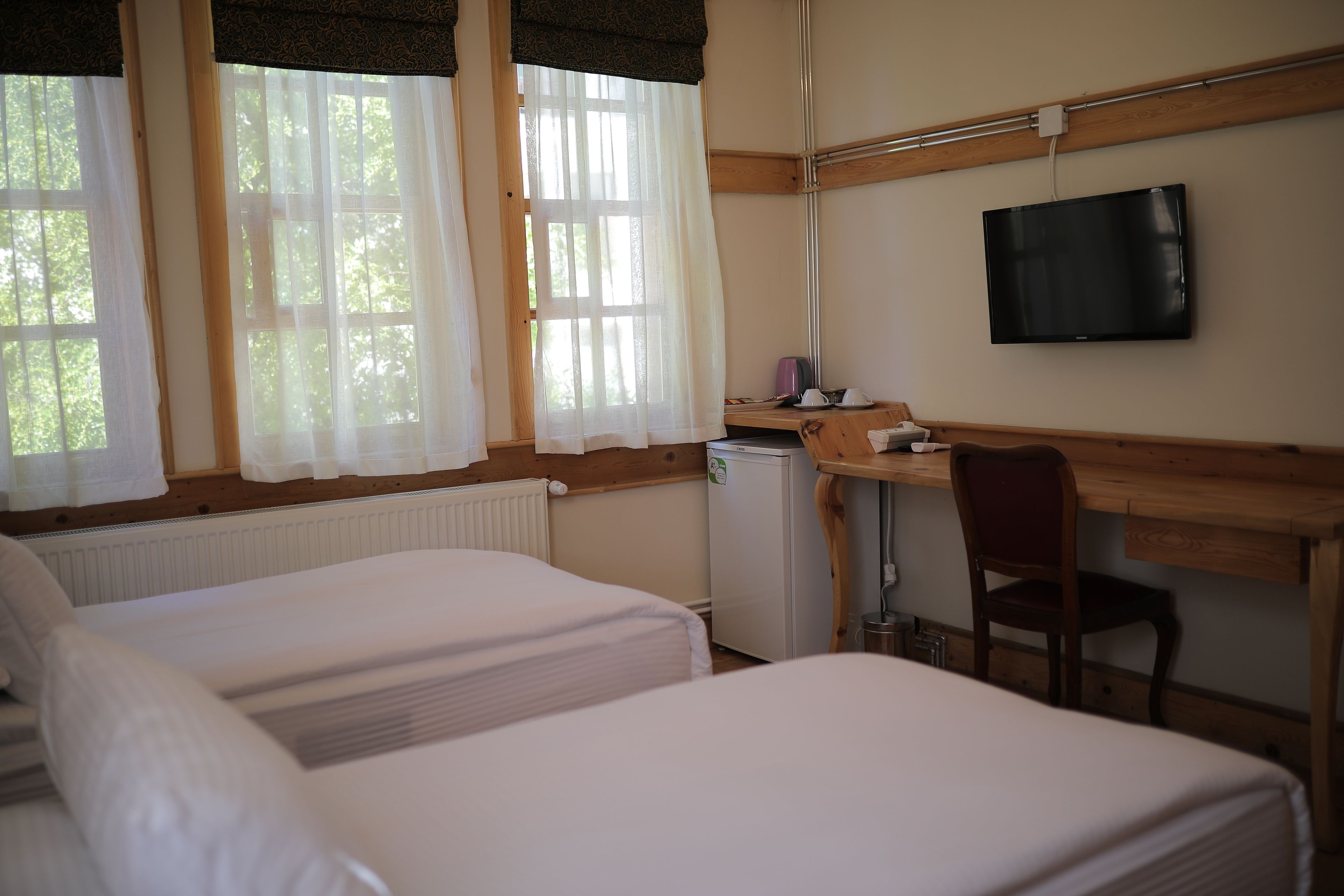 A room with two beds, a desk, a chair, a television, and a small refrigerator.