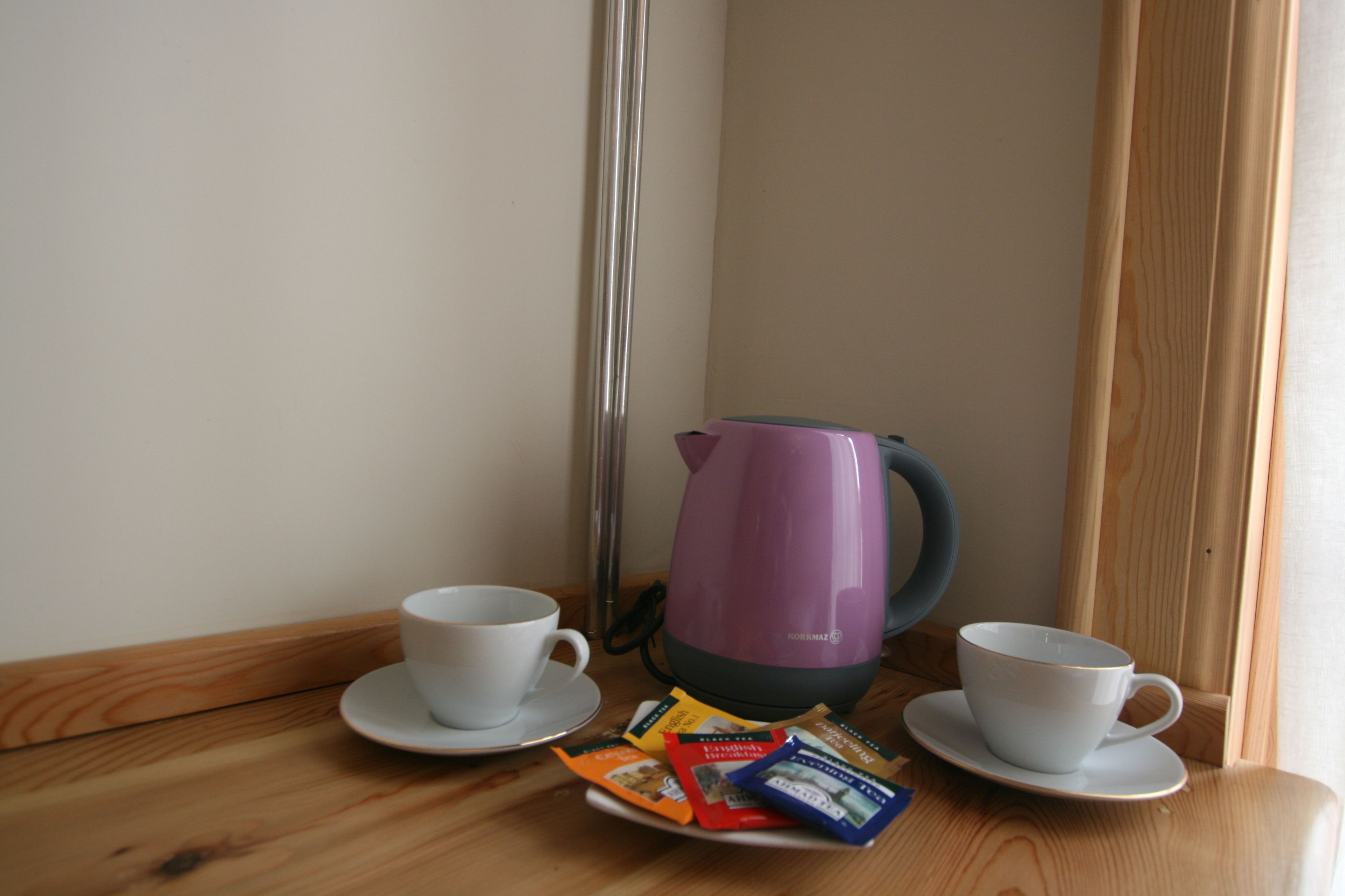 A wooden table with two white cups and saucers, a purple electric kettle, and packets of tea or coffee.
