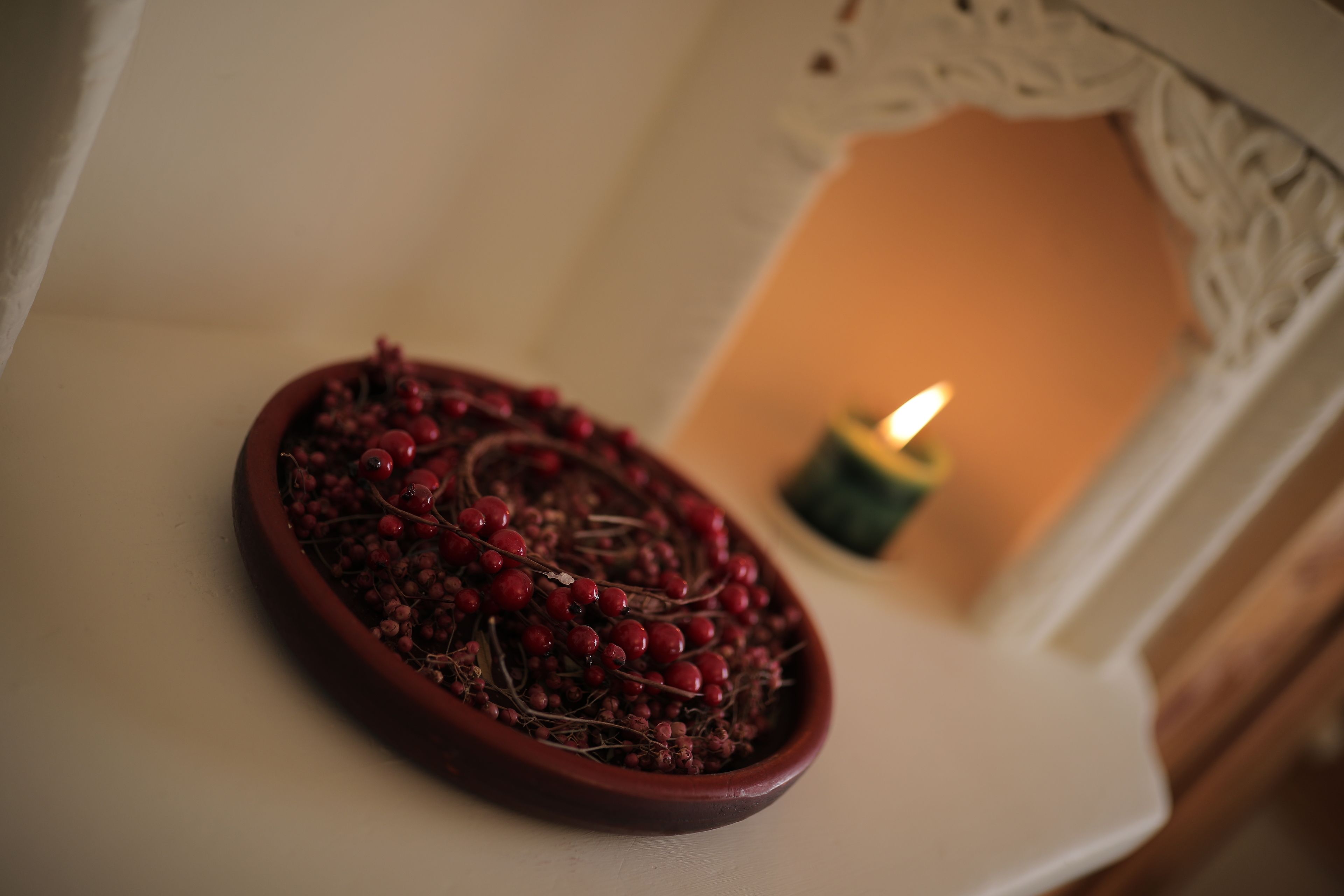 A ceramic dish with red berries and twigs on a white surface.