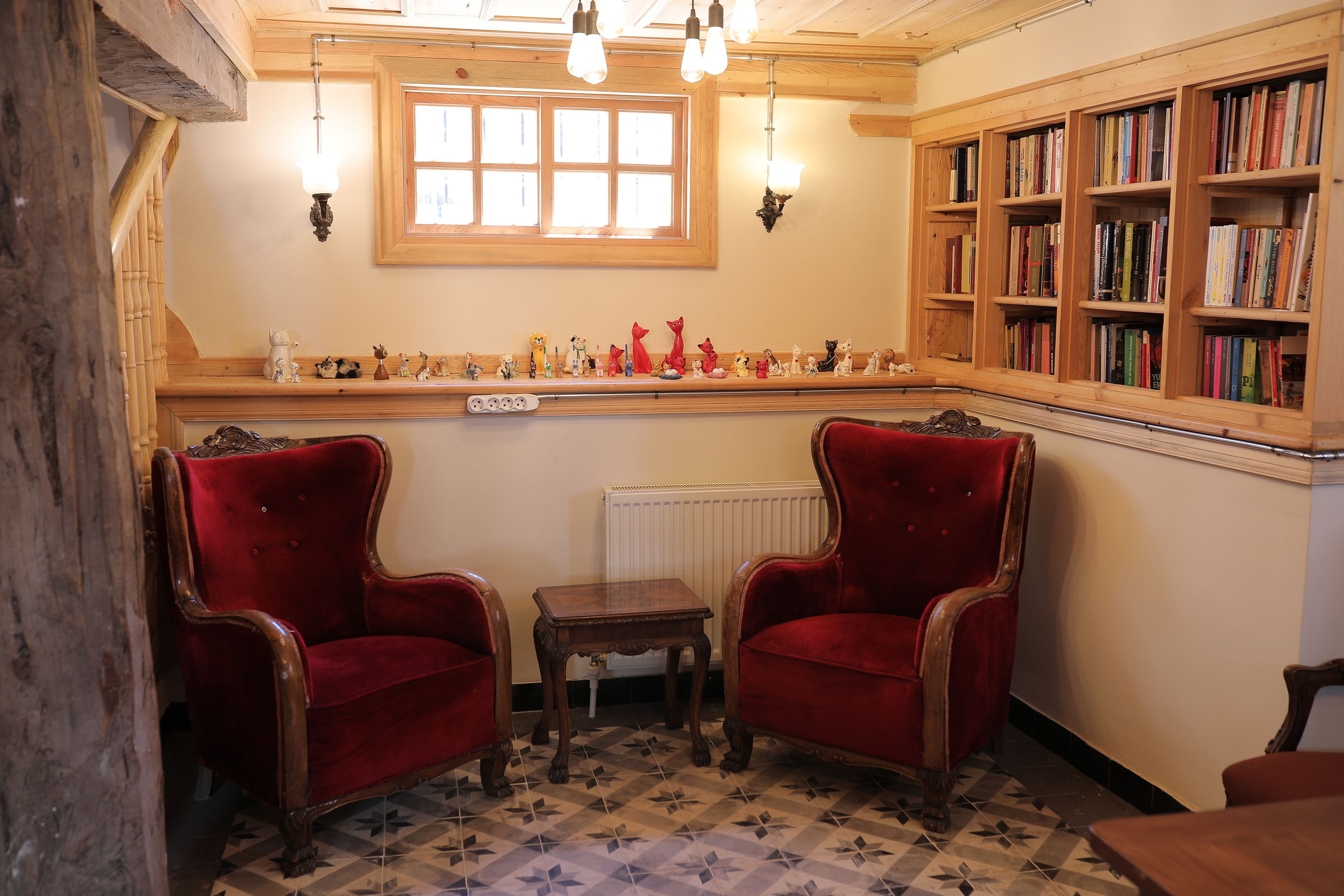 Een kamer met twee rode fluweel fauteuils, een klein houten tafeltje, een radiator en een boekenplank vol boeken.