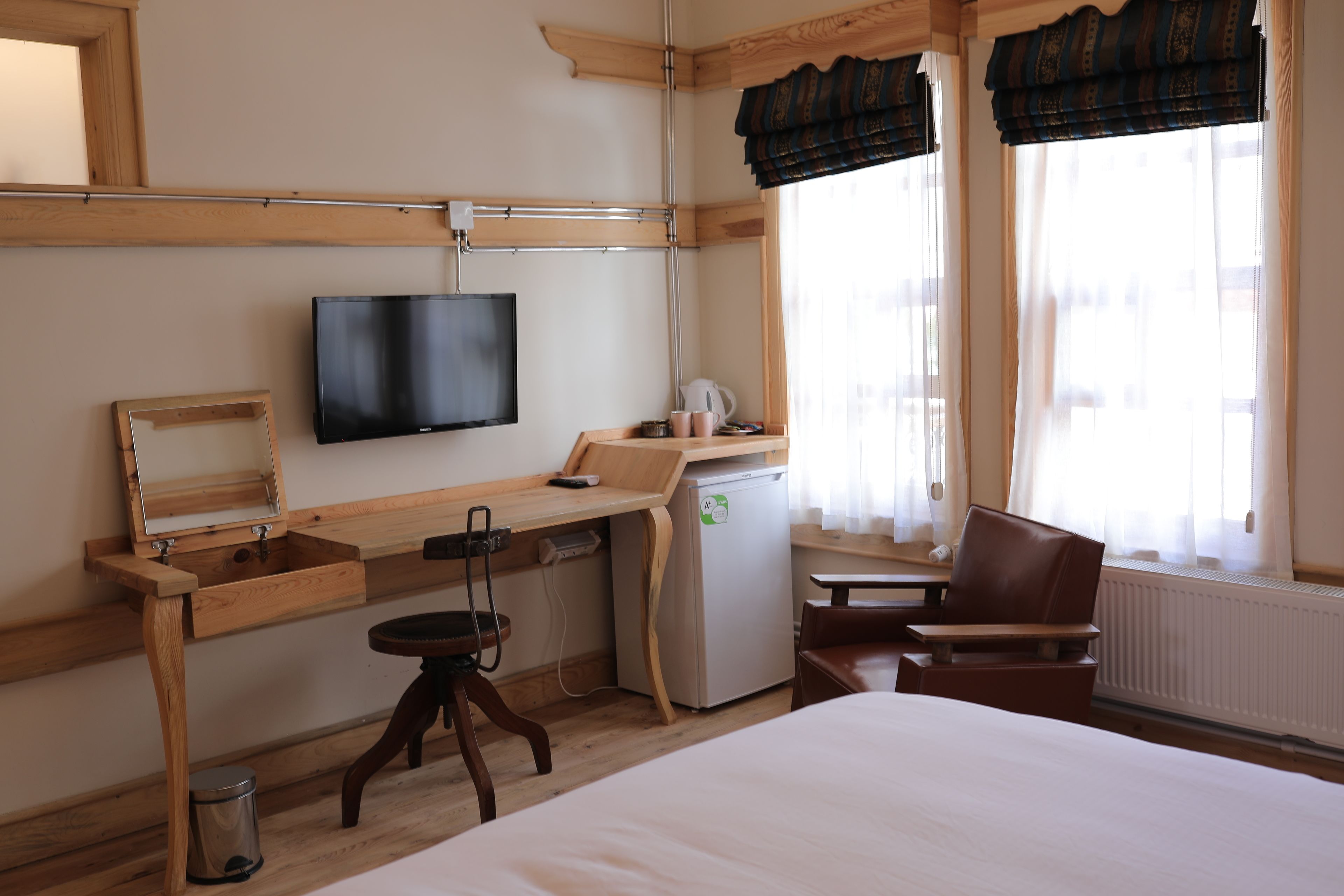 A hotel room with a bed, a desk with a television, a small refrigerator, a chair, and a window with curtains.
