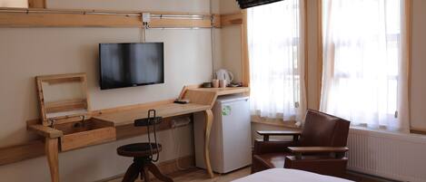 Habitación de hotel con cama, escritorio con televisor, refrigerador pequeño, una silla y ventana con cortinas.