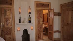 A bedroom with wooden doors, a bed, a nightstand, and a shelf with decorative items. - Melekli Konak (Amasya)