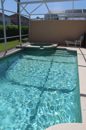 A rectangular swimming pool with clear blue water, surrounded by a white deck and a covered area with two lounge chairs.