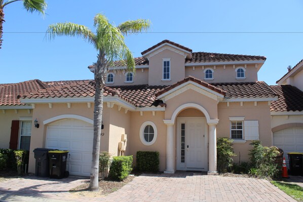 A two-story house with a tiled roof, a front garage, and a palm tree.