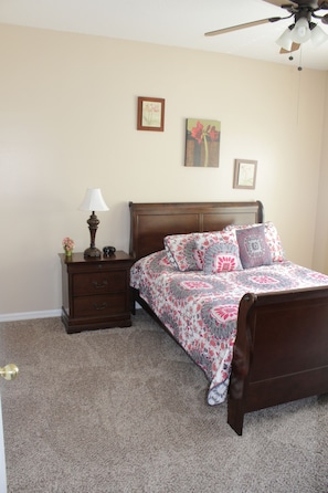 A bedroom with a wooden bed, a nightstand with a lamp, and a ceiling fan.