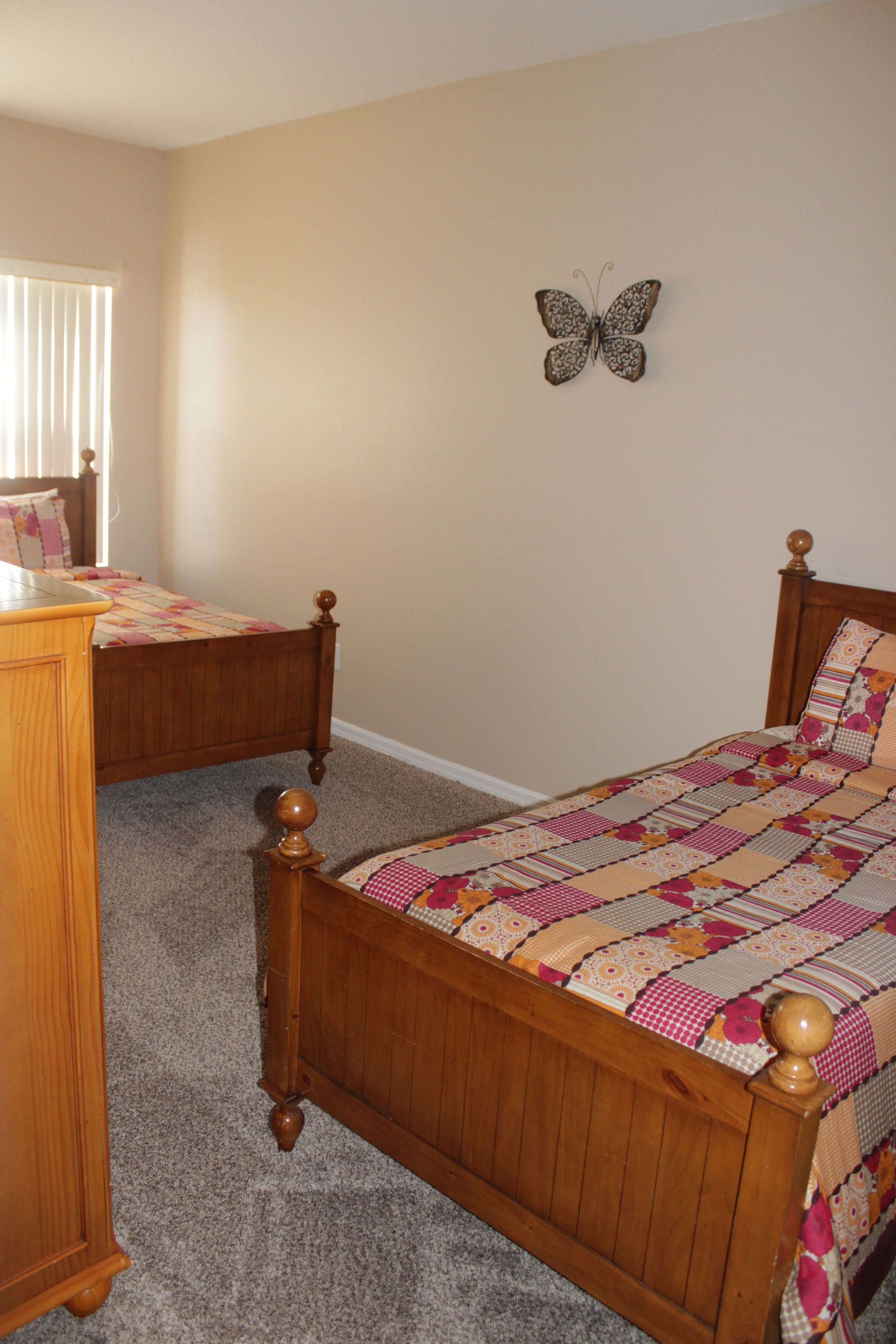 A bedroom with two wooden beds, a wooden dresser, and a butterfly wall decoration.