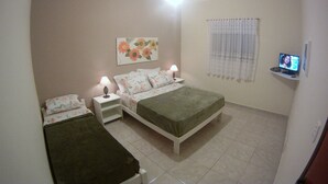 A bedroom with a bed, two bedside tables with lamps, a ceiling fan, a TV on a shelf, and a floral painting on the wall. - Pousada Golden House (Aguas de Sao Pedro)