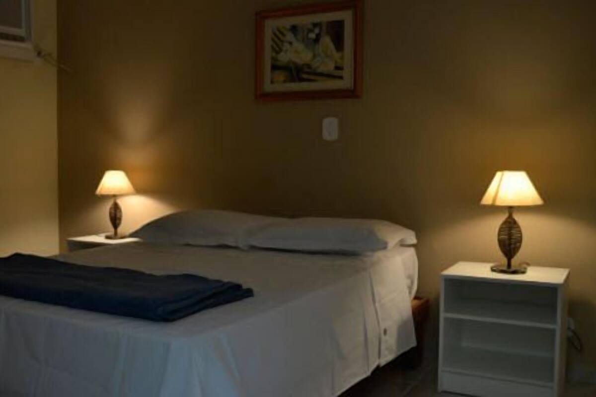 A single bed with a blue blanket, two bedside lamps, a nightstand, and a framed picture on the wall.
