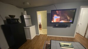 A living room with a flat-screen TV mounted on the wall, a black refrigerator, a white washing machine, and a wooden floor. - Auburn Motel (Auburn)