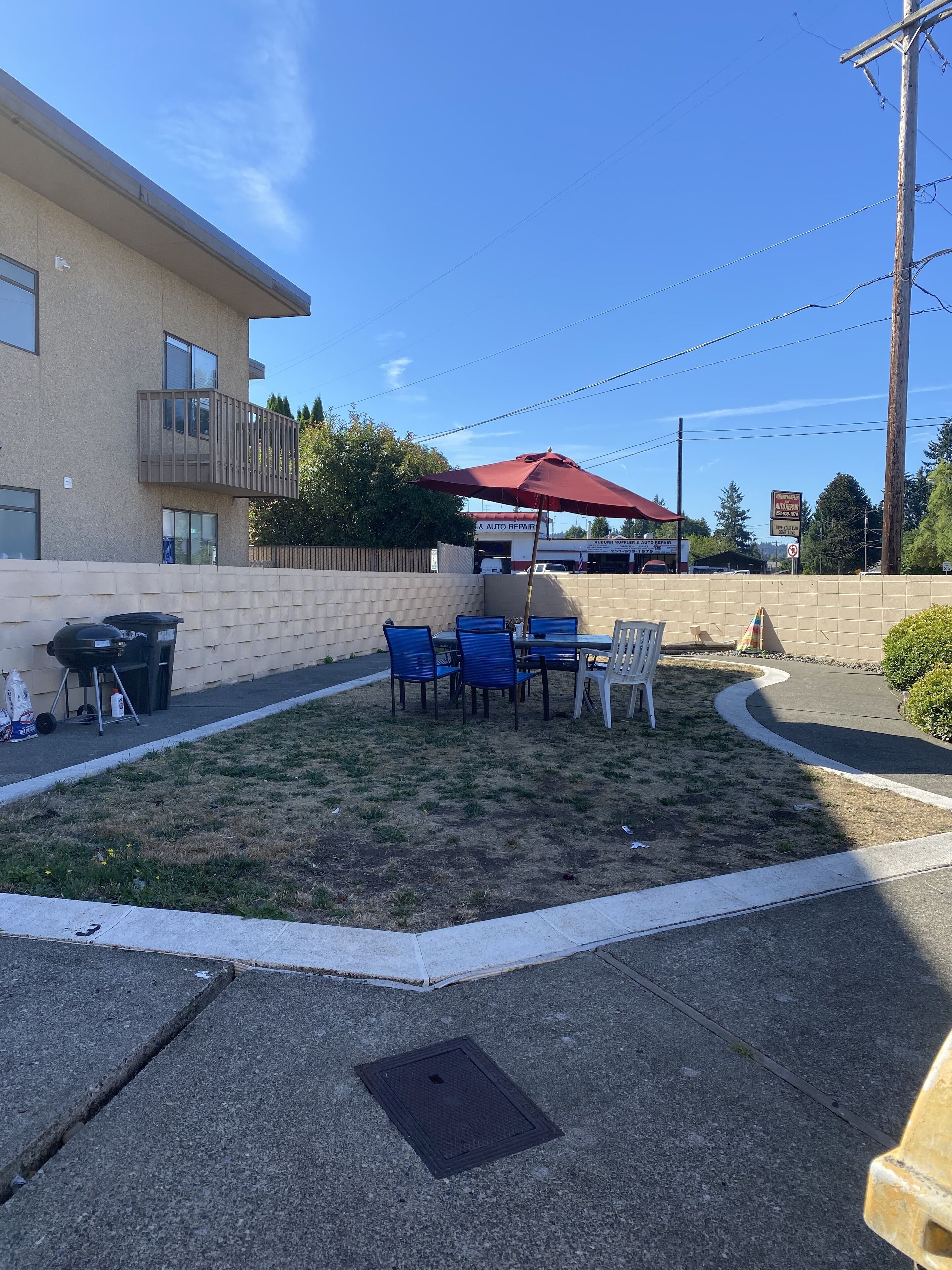 An outdoor patio with a table and chairs, a barbecue grill, and a red umbrella.