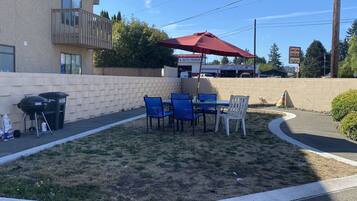 An outdoor patio with a table and chairs, a barbecue grill, and a red umbrella.