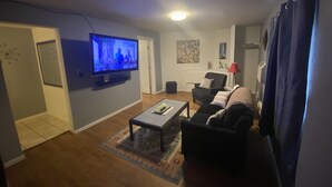 A living room with a flat-screen TV, a sofa, a coffee table, and a patterned rug. - Auburn Motel (Auburn)