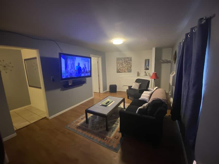 Una sala de estar con televisión de pantalla plana, un sofá, una mesa de centro y una alfombra estampada.