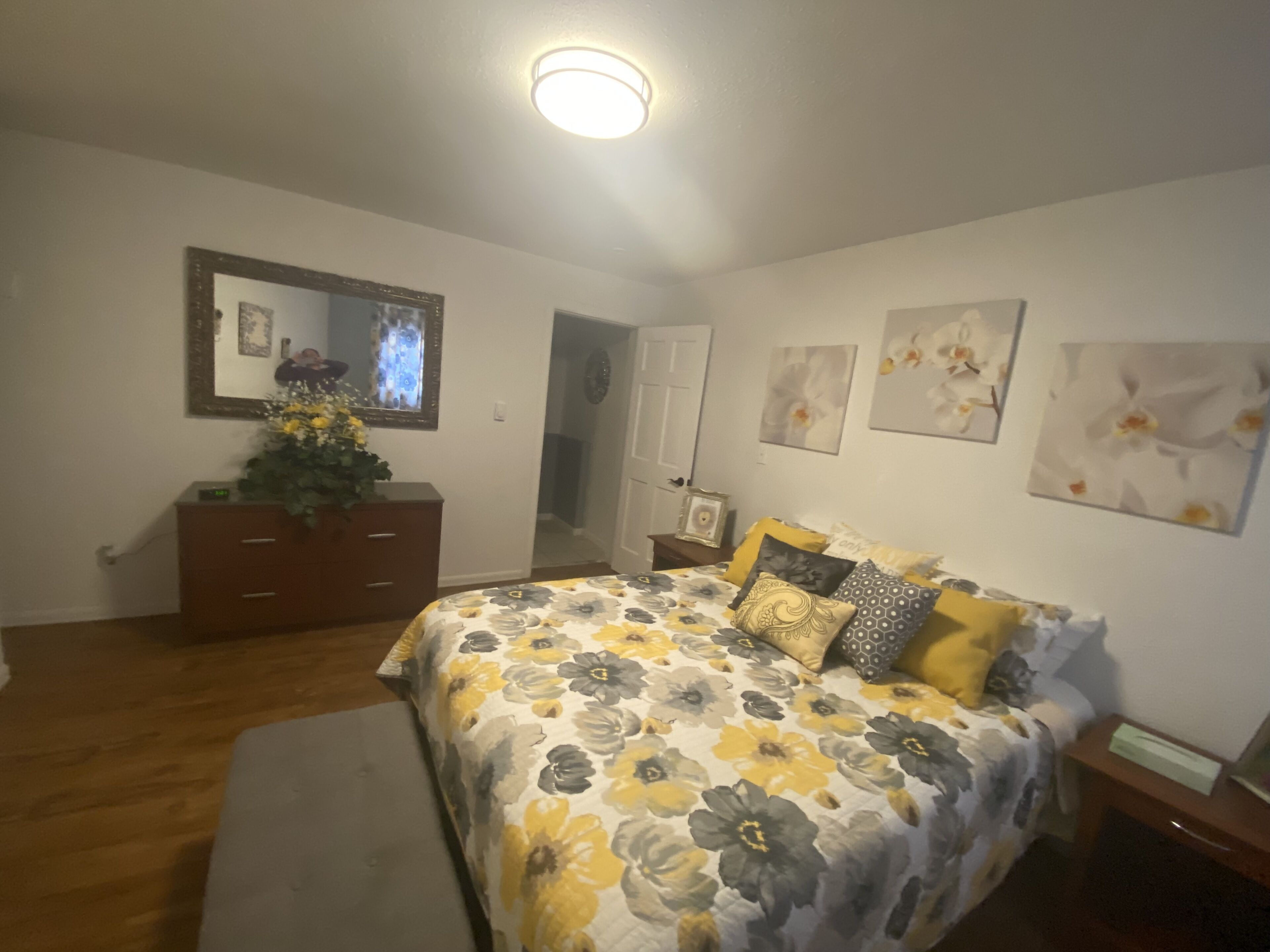 A bedroom with a floral bedspread, a dresser, a mirror, and wall art.