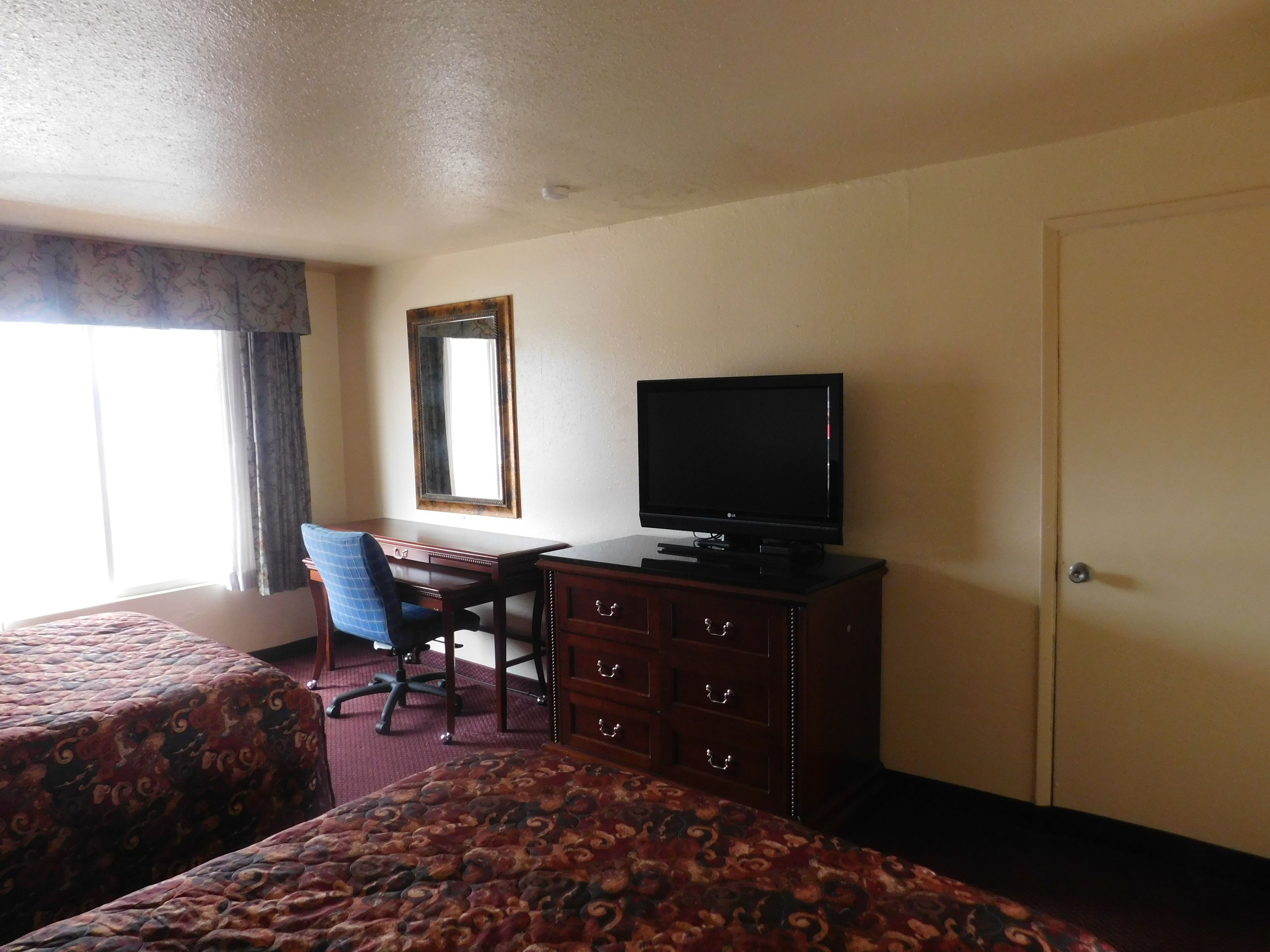 A hotel room with two beds, a desk with a television, a chair, and a dresser.