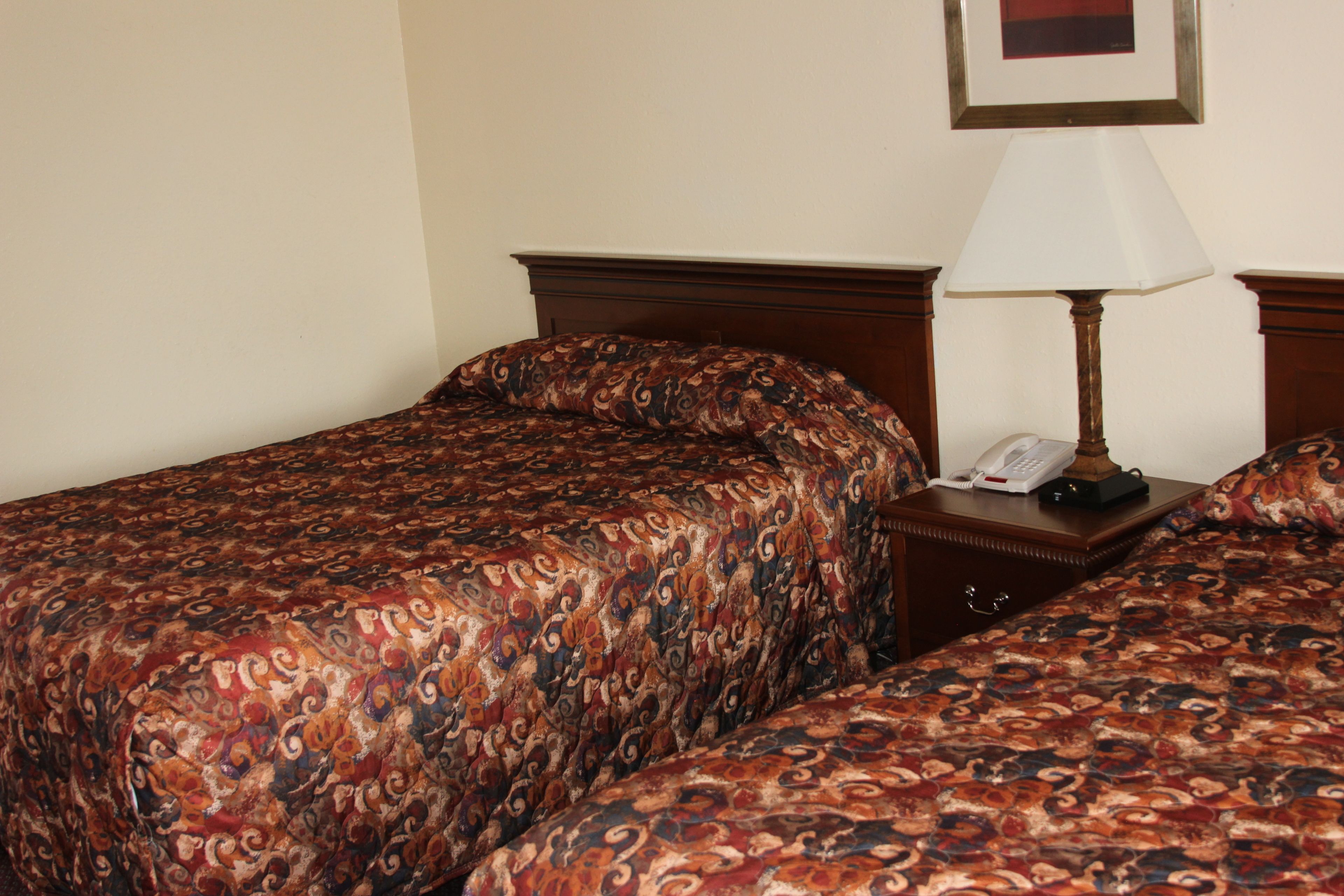 A hotel room with two beds, a bedside table with a lamp, and a framed picture on the wall.