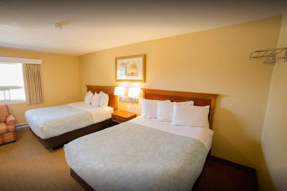 Una camera d'albergo con due letti, una sedia, un comodino e un quadro appeso al muro.