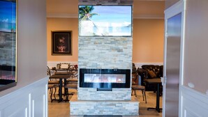 Una sala de estar con chimenea de piedra, un televisor montado encima y una zona de comedor con mesa y sillas.