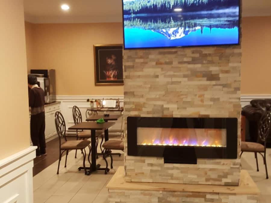 A living room with a stone fireplace, a flat-screen TV mounted above it, and a dining area with chairs and a table.