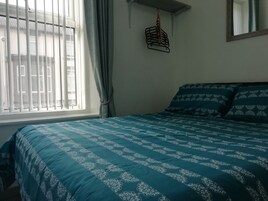 Een slaapkamer met een bed, een raam met zonwering en een hanglamp.