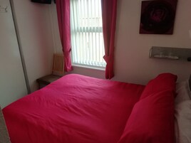 Een slaapkamer met een groot bed, een raam met zonwering, een stoel en een wandplank.