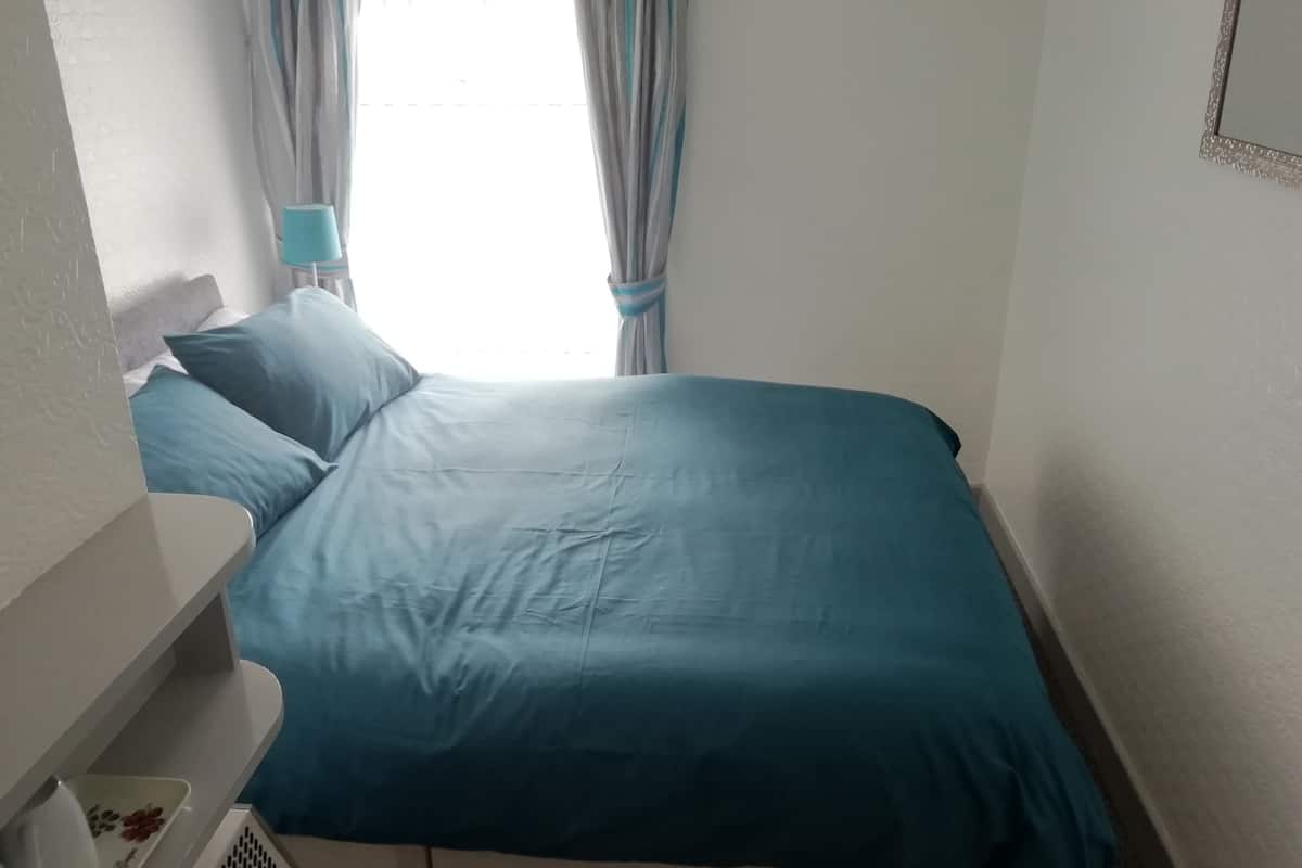 A bedroom with a bed, pillows, a nightstand, and a window with curtains.