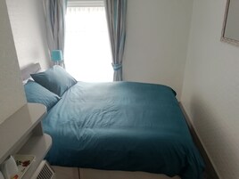 Een slaapkamer met een bed, kussens, een nachtkastje en een raam met gordijnen.