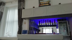 A bar area with a blue-lit shelf displaying various bottles, a sign indicating visitor accommodation, and a window with blinds. - The Shining Diamond (Blackpool)
