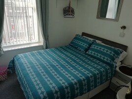 Een slaapkamer met een bed, een nachtkastje, een raam met gordijnen en een wandlamp.