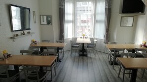A dining area with multiple tables and chairs, a large window with blinds, and a mirror on the wall. - The Shining Diamond (Blackpool)
