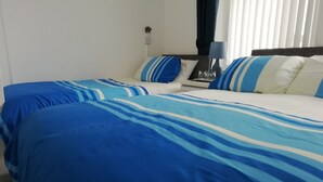 A hotel room with two beds, each with blue and white striped bedding. There is a nightstand with a lamp and a glass of water. - The Shining Diamond (Blackpool)