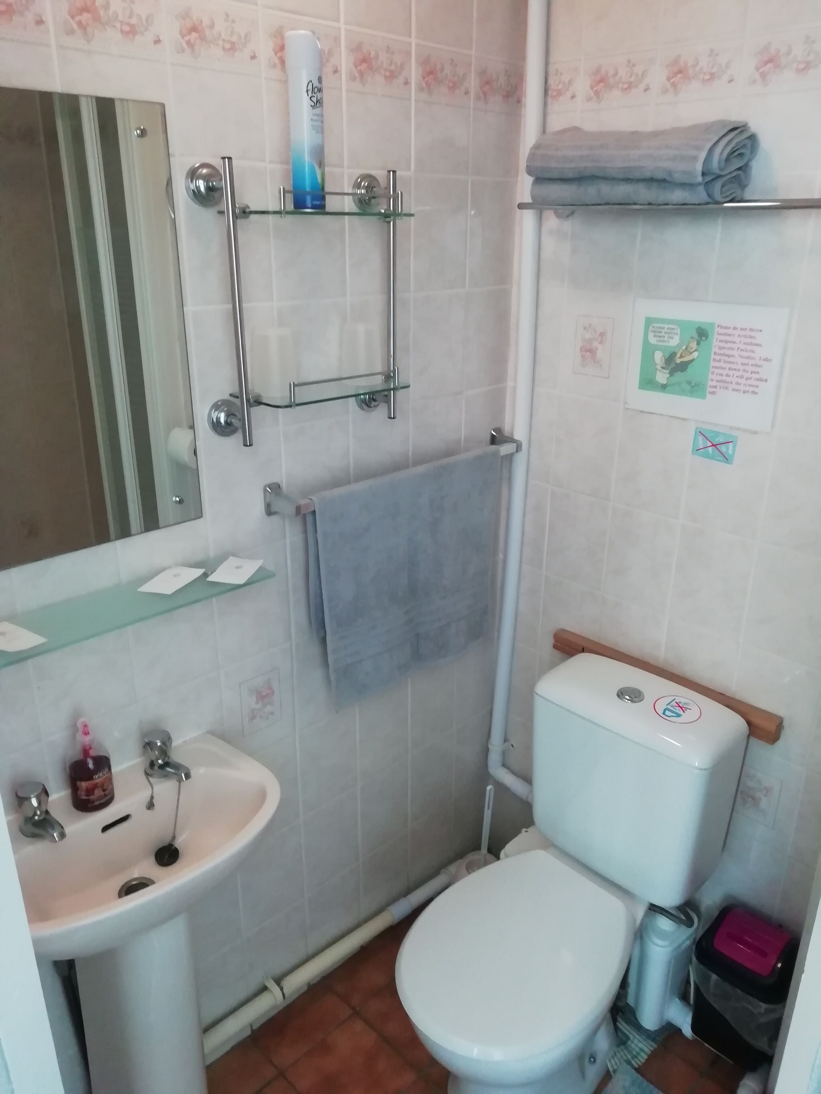 A small bathroom with a toilet, sink, and shower. There are toiletries on the sink and a towel on the wall.