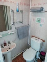 A small bathroom with a toilet, sink, and shower. There are toiletries on the sink and a towel on the wall.