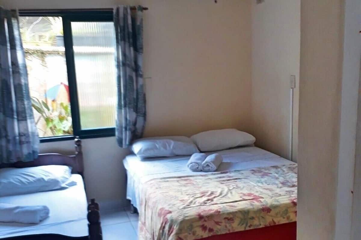 A small, clean room with a bed, a chair, and a window.