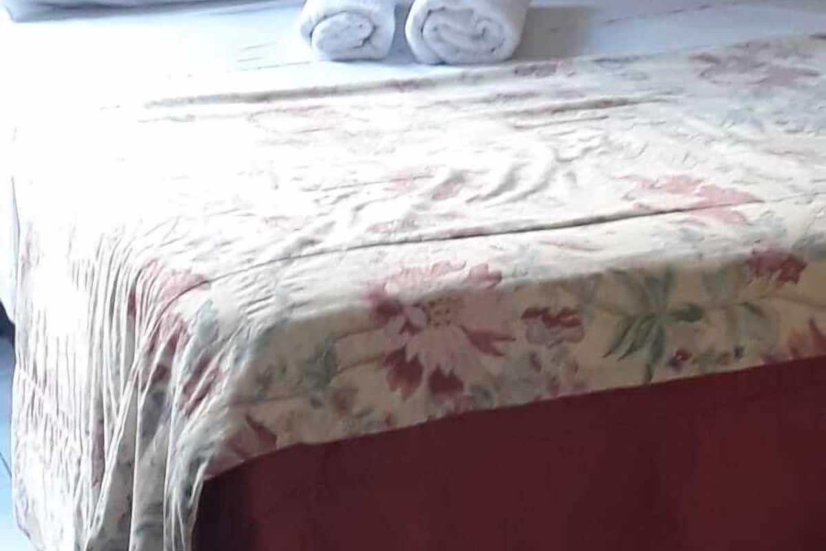 A bed with white linens and two rolled towels on it.