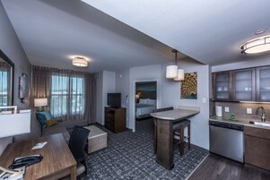 A compact hotel room with a kitchenette, a sofa, a dining table, a bed, and a bathroom.