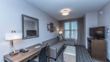 Habitación de hotel con escritorio, sofá, televisor y un mueble pequeño.