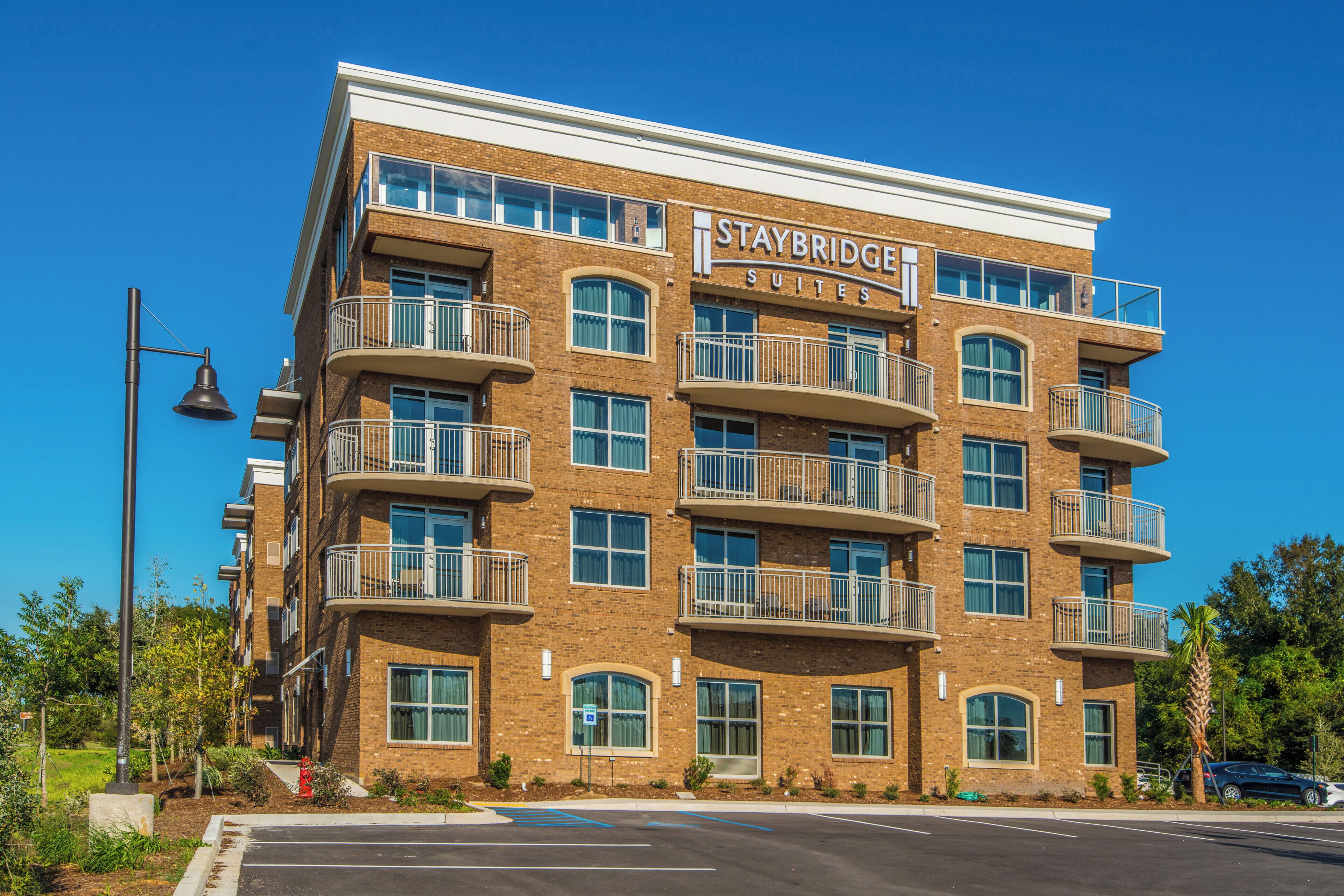 Un hotel Staybridge Suites de varios pisos con balcones, ventanas amplias y un cielo azul despejado.