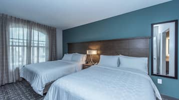 A hotel room with two beds, a nightstand with a lamp, a large mirror, and a window with curtains.